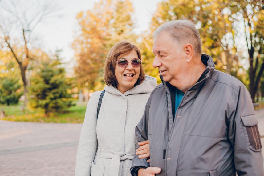 A couple walks arm in arm down a sidewalk in autumn.