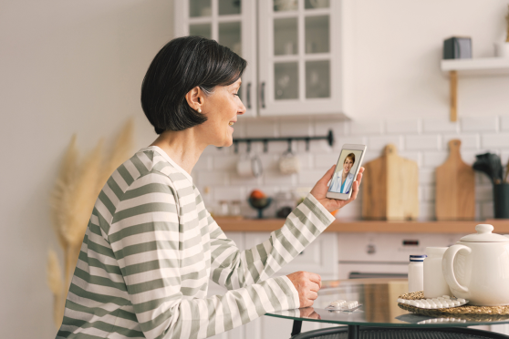 Woman holding her phone in her kitchen, on a video call with a doctor